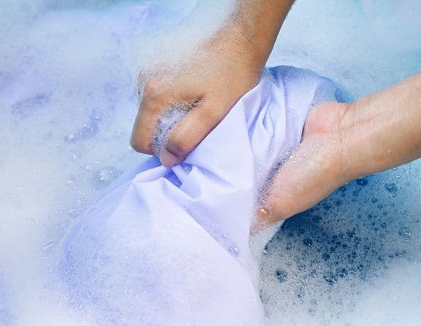person applying detergent to remove oil stain from clothes close up